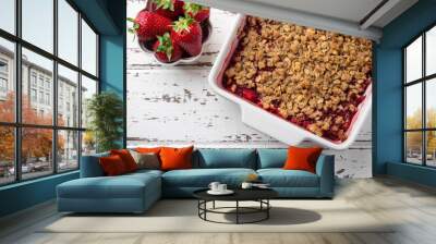 Homemade strawberry and rhubarb crumble served with fresh berries on light wooden background; Overhead shot Wall mural