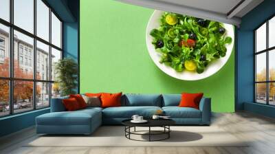 fresh salad of arugula and valerian leaves with colored tomatoes and blueberries in a plate on a green background. Wall mural