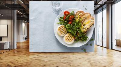 grilled Italian Tomino cheese served on a table with arugula salad and fresh homemade ciabatta bread and tomato on a blue linen festive tablecloth. summer menu Wall mural