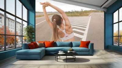 a young girl stretches on the road before running. Brunette leads a healthy lifestyle Wall mural