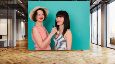 Two young beautiful woman touch with powder brush on blue background Wall mural