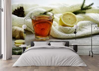 Glass cup of tea with lemon and ginger root slices, mint leaf on glass saucer on a rustic wooden table on background of the women's woolen mittens and knitted scarf outdoor Wall mural