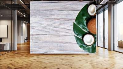 two halves of coconut and one whole coconut with a leaf of tropical monstera plant on a white wooden background. Flat layer, top view, copy space. Creative concept of healthy eating. horizontal photo Wall mural