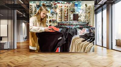 Shopping concept .teenager girl tries on and buys a sports shirt in the mall. A large selection of clothes in the store, black Friday sales. Showcase with sunglasses Wall mural