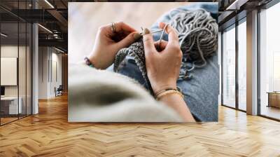 Close-up of hands knitting with gray yarn, focusing on a cozy winter craft. Relaxing and mindful activity during colder months. Wall mural