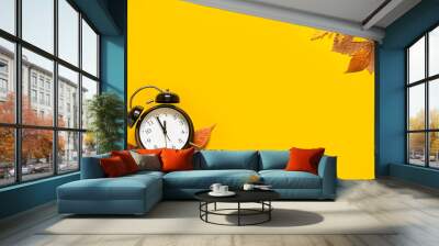 Daylight saving day. Fall Back. Black Alarm clock and autumn leaves on yellow background. Daylight saving time end Wall mural