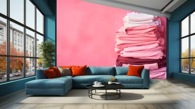 Fast fashion, Overconsumption, trends in fashion industry. Stack of pink clothing on pink background. Pile of trendy pink shirts, dresses and sweaters, pink wall background. Wall mural