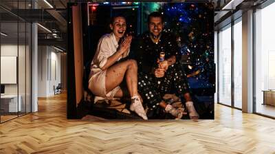 Merry Christmas and happy new year. Young couple in love celebrating Christmas or new year eve at home. Romantic couple in pajamas having fun with confetti at home. Wall mural