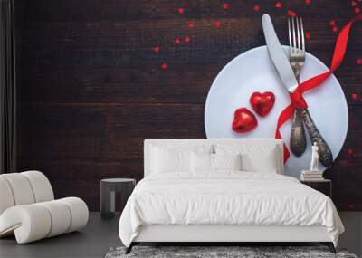 Valentine's Day Festive table setting, flat lay with two red heart shape chocolate candies on white plate, fork, knife and red ribbons on wooden table. Valentine Day, love, dating concept, copy space Wall mural