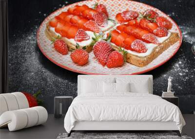 An image of a plate with two strawberry sandwiches, a cutting board with sliced and whole strawberries, powdered sugar around on a black wooden table Wall mural