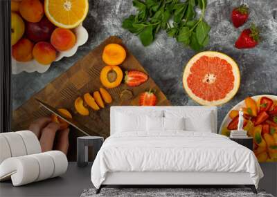 Chopping fruit salad on wooden cutting board. Healthy tasty food on dark concrete background. Ingredients for fruit salad. From above, flat, overhead. Wall mural