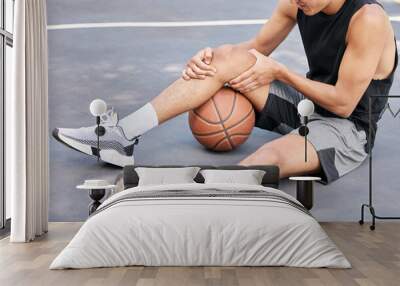 Basketball, man and knee in sports injury on the court holding painful, sore or tender area in the outdoors. Basketball player suffering from leg pain, joint or inflammation in sport match or game Wall mural