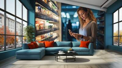 A beautiful young woman buys groceries in a supermarket and uses her smartphone to make healthy choices. Wall mural