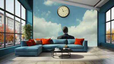 A businessman stands with his back and looks at a round wall clock against the sky. Wall mural