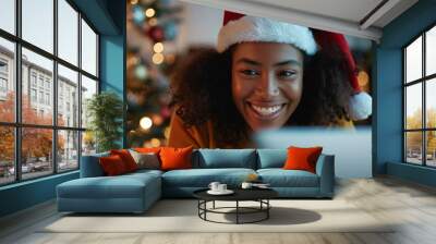 A cheerful woman celebrates the Christmas holidays at home, sitting with a laptop, smiling with joy. Wall mural