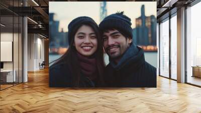 A couple is smiling for the camera in front of a city skyline. The woman is wearing a red scarf and the man is wearing a black hat Wall mural