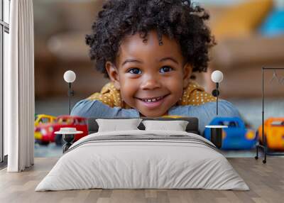 A cute black boy smiles joyfully with colorful toy cars lined up. Wall mural