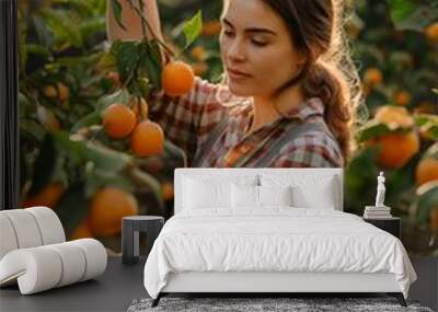 A woman is picking oranges from a tree. She is wearing a plaid shirt and overalls Wall mural