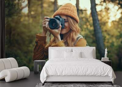 A woman wearing a yellow jacket and a brown hat is taking a picture of a forest. She is smiling and she is enjoying the moment Wall mural