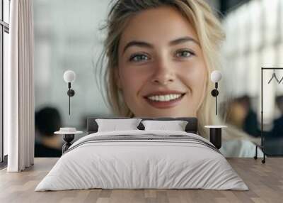 A woman with blonde hair and blue eyes is smiling and wearing a white shirt. She is sitting in front of a window Wall mural