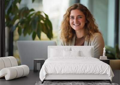 A woman with curly hair is sitting at a desk with a laptop in front of her. She is smiling and she is enjoying her work Wall mural