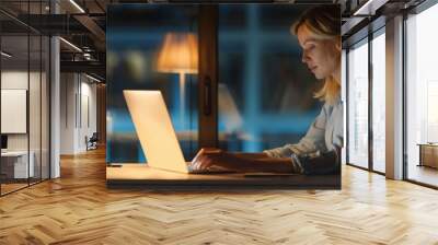 A young businesswoman working late at her office desk, using a laptop. Wall mural