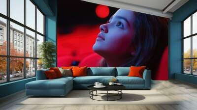 A young girl is sitting in a red chair in a dark theater. She is looking up at the screen with a look of wonder on her face Wall mural