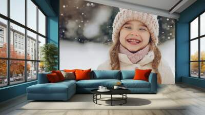 A young girl wearing a white hat and a pink scarf is smiling in the snow. She looks happy and content Wall mural