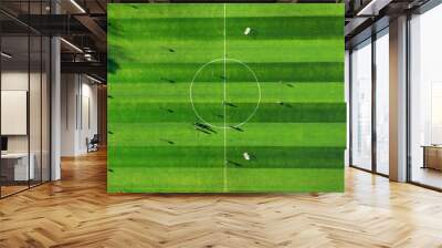 Aerial view of a soccer field with players and shadows. An aerial view of a soccer field with vivid green grass and a clearly marked center circle. Wall mural