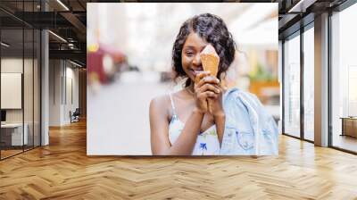 Attractive african playful woman on the street having fun and eating ice cream. Dreaming outdoor summer portrait of millennial black girl in straw hat, blue jeans jacket enjoying summer. Wall mural