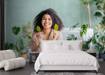 Beauty portrait of playful woman in bathroom covering her eyes with lemon tree leaves in hand with green plants on background. Skincare, cleansing, eco, organic, zero waste, reduce, reuse, recycle. Wall mural