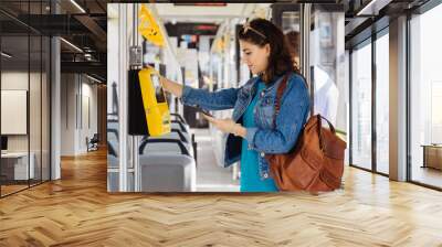 Brunette womanstudent paying with smartphone for the public transport in the tram or bus. Wall mural