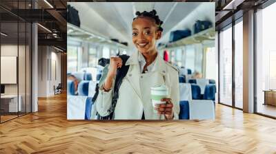 Business trip travel long short distance public transport concept. Portrait of african female traveler In white jacket with backpack smiling drinking coffee on train indoor. Wall mural