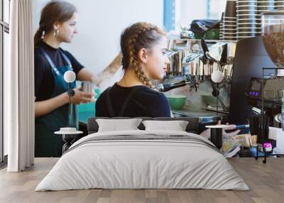 Cafe staff at work concept. Team of two young women barista in black t-shirt and green aprons working together, preparing cappuccino or latte with coffee machine in workplace cafeteria modern interior Wall mural