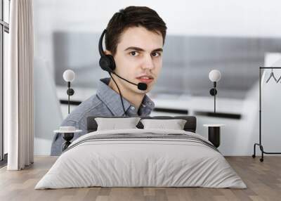 Casual dressed young man using headset and computer while talking with customers online. Call center, business concept Wall mural