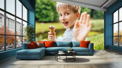 Cute school age blond boy sitting on lake side, relaxing, eating ice cream at summer day outdoor. Wall mural