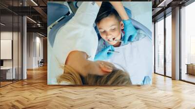 Female dentist very carefully check up and repair tooth of her young male patient. Wall mural