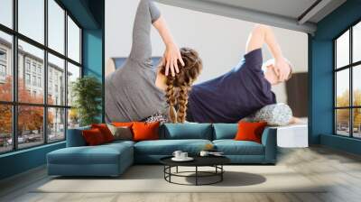 Gorgeous woman instructor performing back exercise on a foam roller at same time with handsome guy at pilates studio. Coach and patient doing fascia exercise on side surface of back. Wall mural