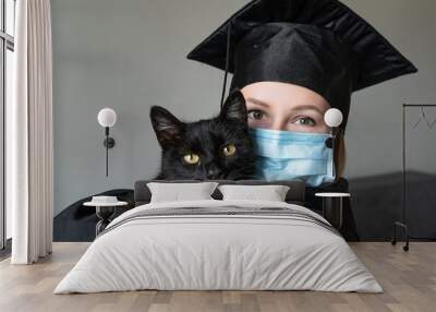 Graduation of a woman with face mask dressed in a black gown and holding a black cat Wall mural