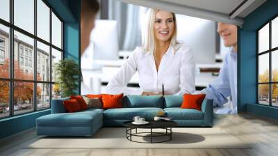 Group of business people discussing questions at meeting. Headshot of blonde businesswoman while smiling to her colleague at office negotiation. Teamwork and cooperation in corporate occupation Wall mural