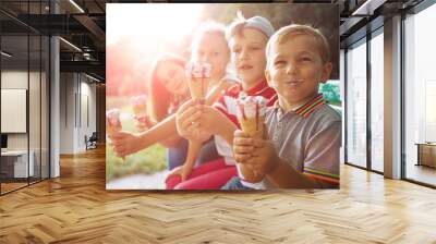 Group of four happy children eating ice cream together outdoor. Photo of happy blond girls with two handsome boys sitting on the bench and smiling at camera. Sun glare effect Wall mural