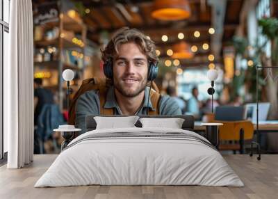 Handsome, cheerful man in a buzzing cafe enjoys music with headphones, blending modern technology and leisure. Wall mural