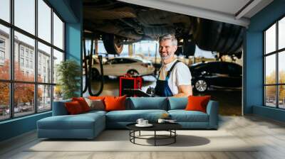 Happy smiling handsome grey hair mechanic at work in his garage. Wall mural