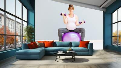 Happy smiling pregnant woman sitting on fitness bal and working with dumbbells. Full body. Sport, maternity and liesure concept. Wall mural