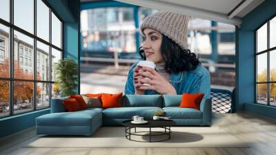 happy young woman drinking take away coffee and waiting for bus at bus station  Wall mural