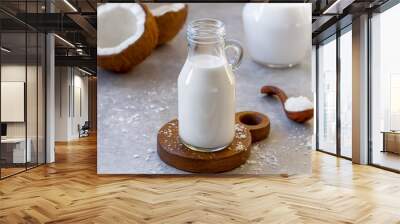 Homemade coconut milk served in glass bottle with fresh coconut and flakes in spoon on background. Selective focus, concrete background, horizontal Wall mural