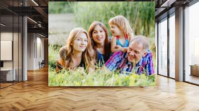 Ideal picture of family happiness - happy family with two daughter having fun and lying on the grass in lake shore on a summer day in sunset. Parenthood, love, vacation and happy family concept. Wall mural