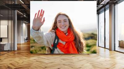 Joyful Woman Waves While Hiking on a Sunny Day in a Lush Green Landscape Wall mural