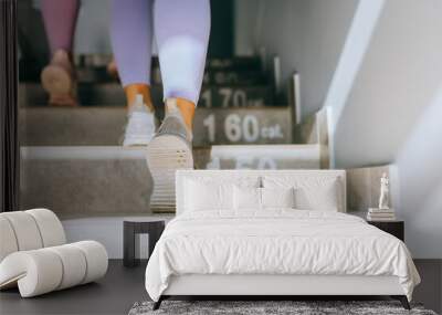 Low angle rear portrait of two unrecognizable female friends go up in action on staircase in fitness studio or gym. Wall mural