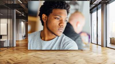 Melancholic headshot portrait of young black man looking aside isolated on blurred indoors background. Wall mural